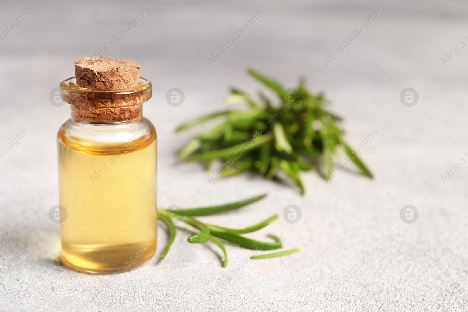 Photo of Bottle with essential oil and fresh rosemary on light textured table, space for text