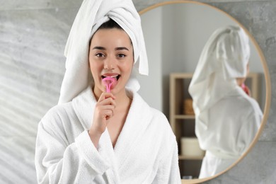 Happy woman brushing her tongue with cleaner in bathroom, space for text