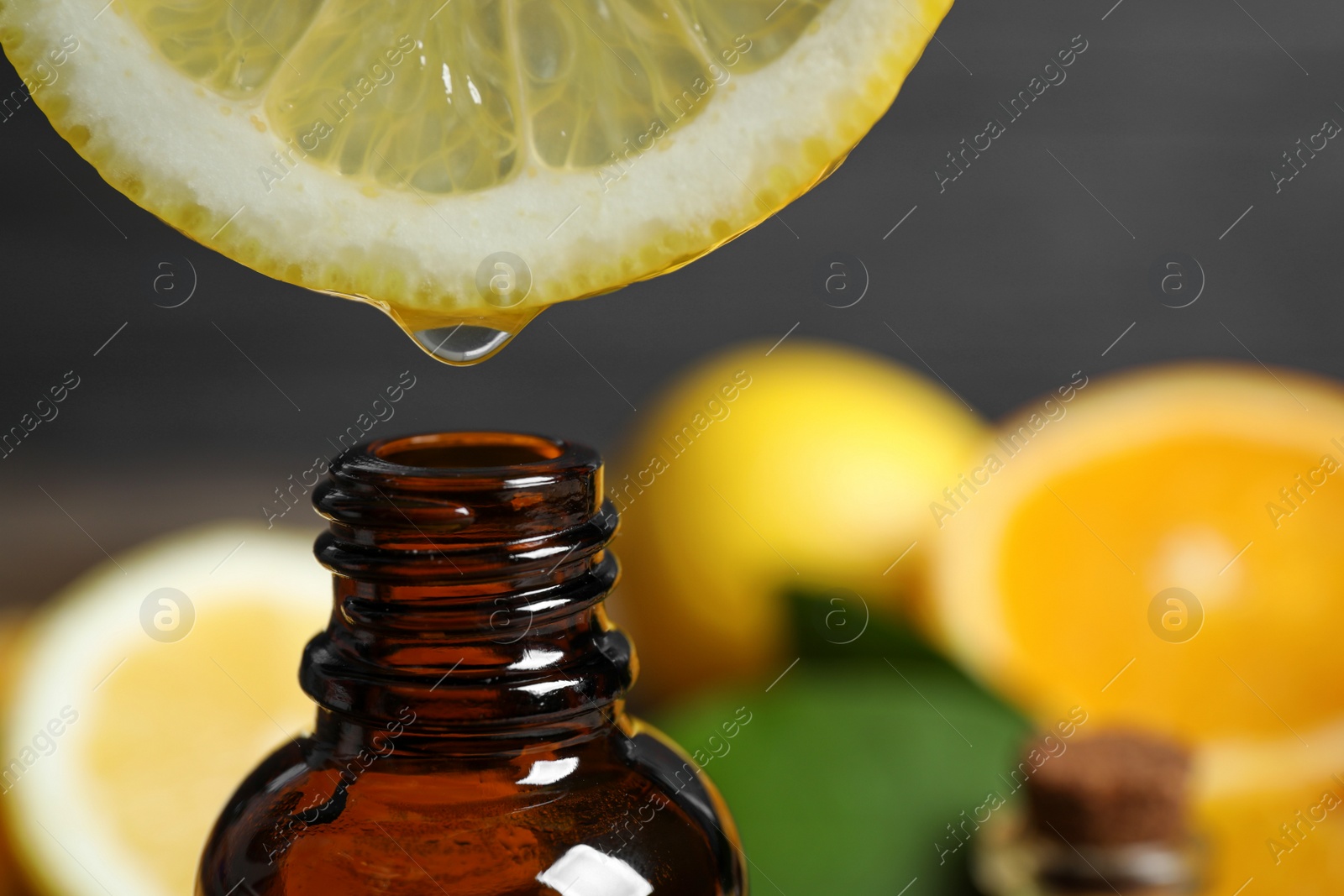 Photo of Citrus essential oil dripping from lemon slice into bottle, closeup