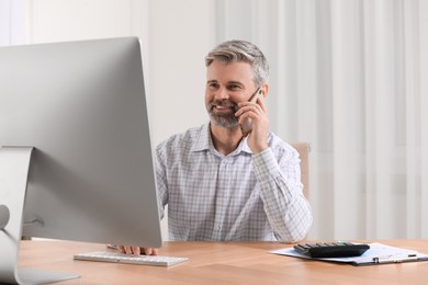 Photo of Professional accountant talking on phone and working at wooden desk in office