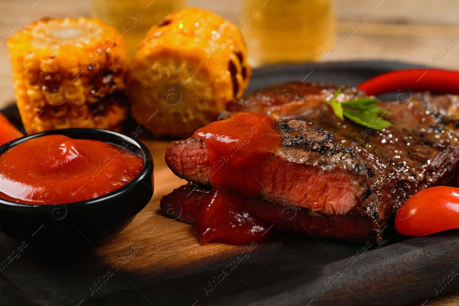 Photo of Delicious fried steak with sauce and grilled corn on wooden table, closeup