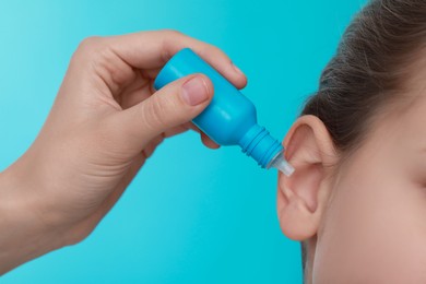 Mother dripping medication into daughter's ear on light blue background, closeup