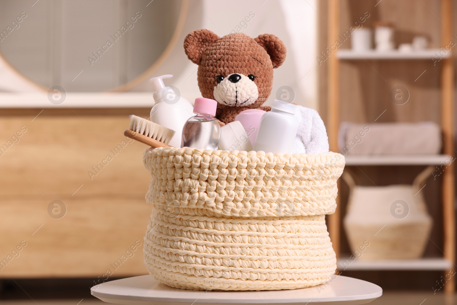 Photo of Knitted basket with baby cosmetic products, bath accessories and toy bear on white table indoors