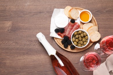 Delicious rose wine and snacks on wooden table, flat lay. Space for text