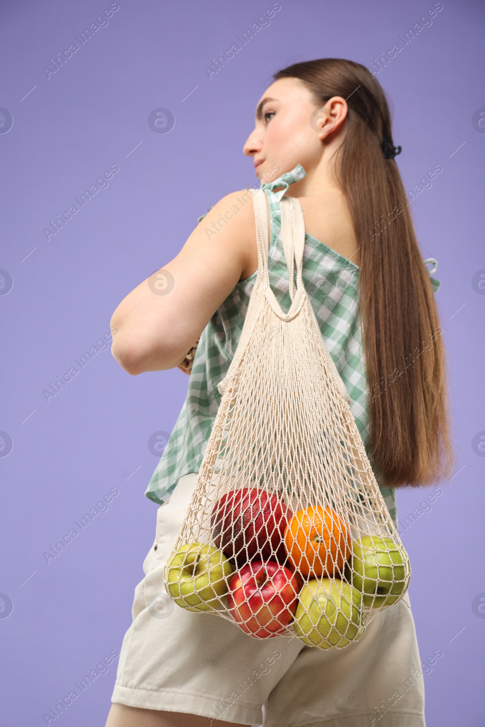 Photo of Woman with string bag of fresh fruits on violet background, low angle view