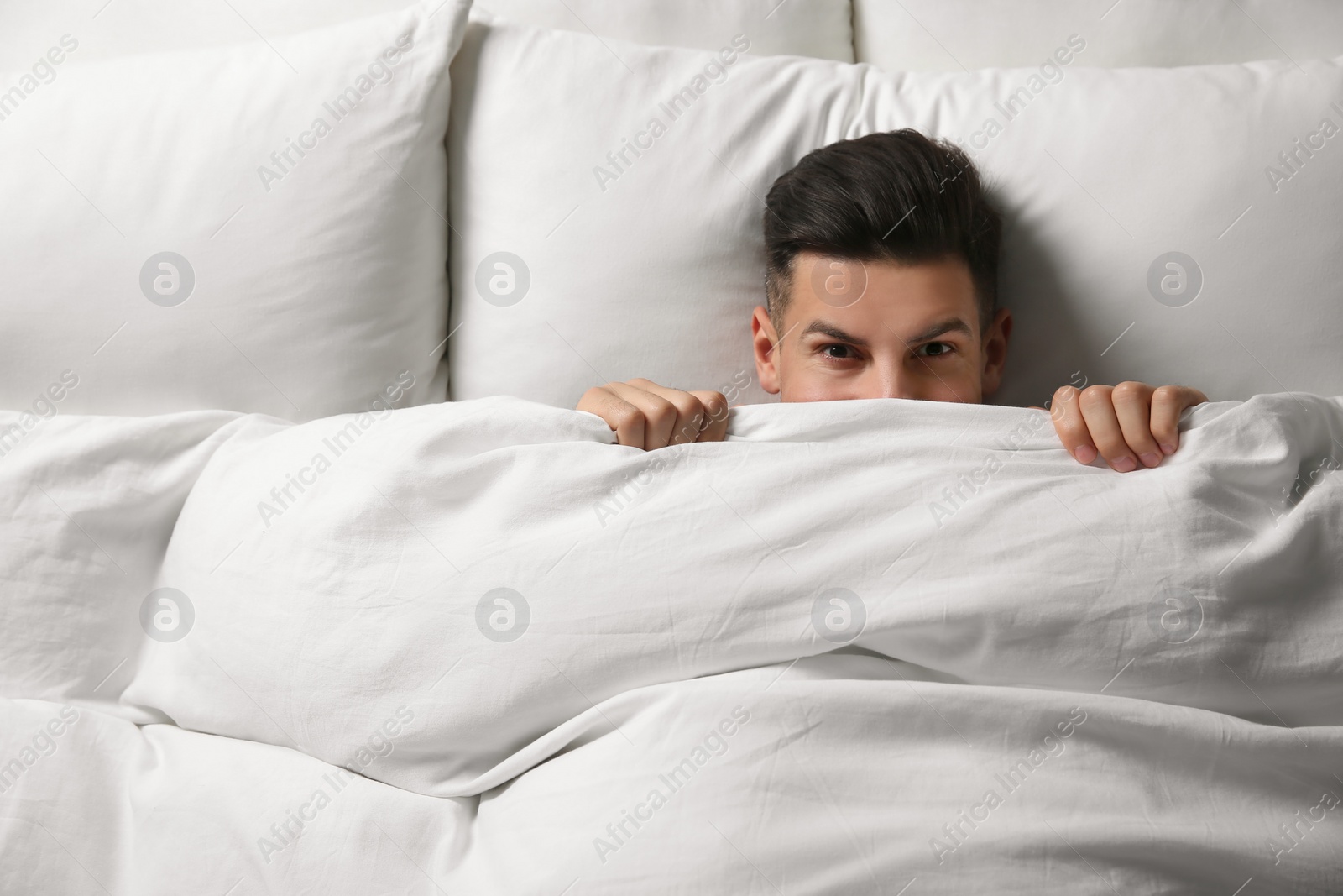 Photo of Handsome man covering his face with blanket while lying in bed at home