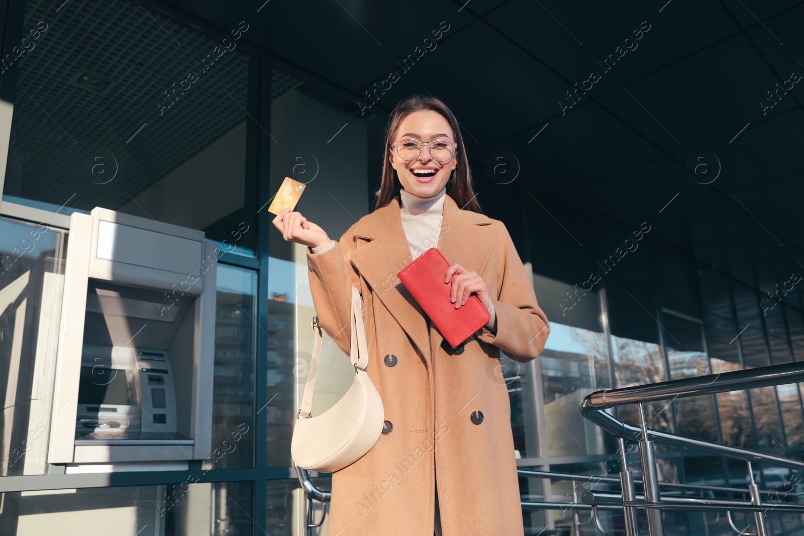 Photo of Excited young woman with credit card near cash machine outdoors