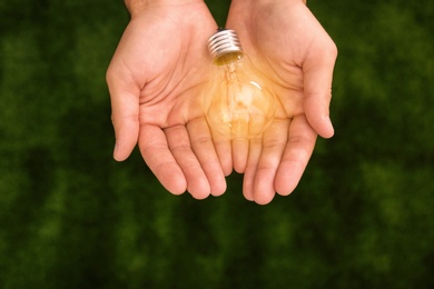 Photo of Man holding lamp bulb against green background, top view