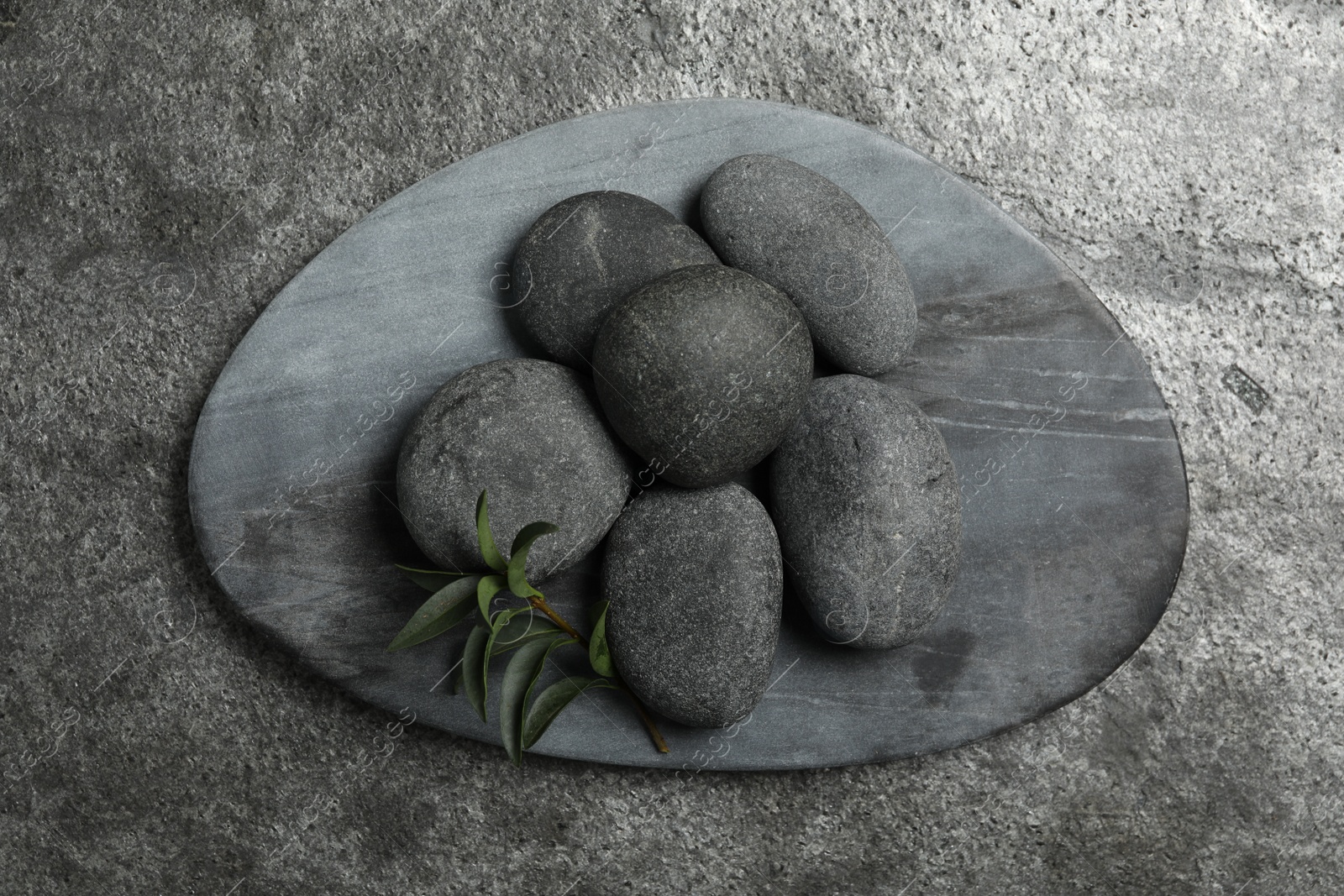 Photo of Spa stones and green leaf on grey table, top view