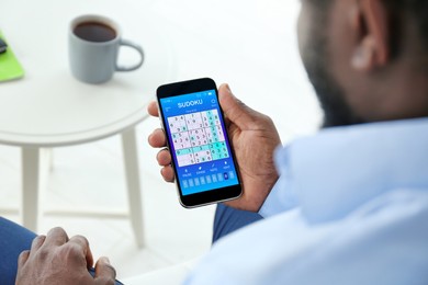 Image of Man playing sudoku game on smartphone indoors, closeup