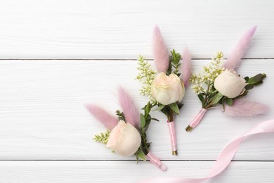 Photo of Small stylish boutonnieres and ribbon on white wooden table, flat lay. Space for text