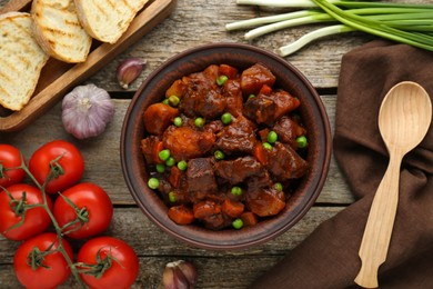 Photo of Delicious beef stew and ingredients on wooden table, flat lay