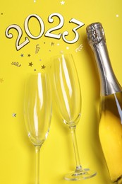 Photo of Happy New Year 2023! Flat lay composition with bottle of sparkling wine on yellow background