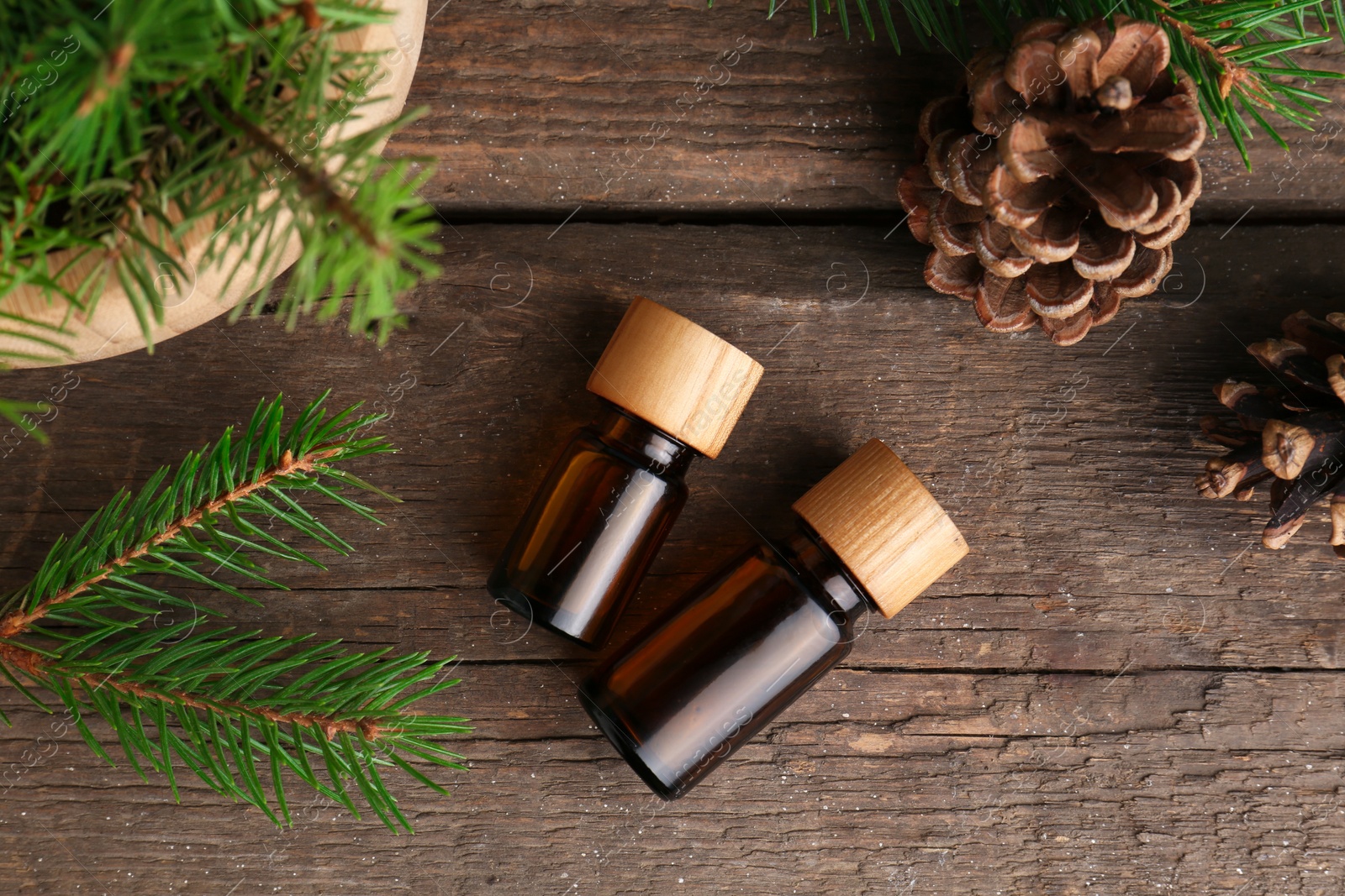 Photo of Bottles of pine essential oil, conifer tree branches and cones on wooden table, flat lay