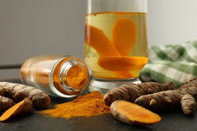 Glass cup of tasty tea, turmeric roots and powder on black textured table, closeup