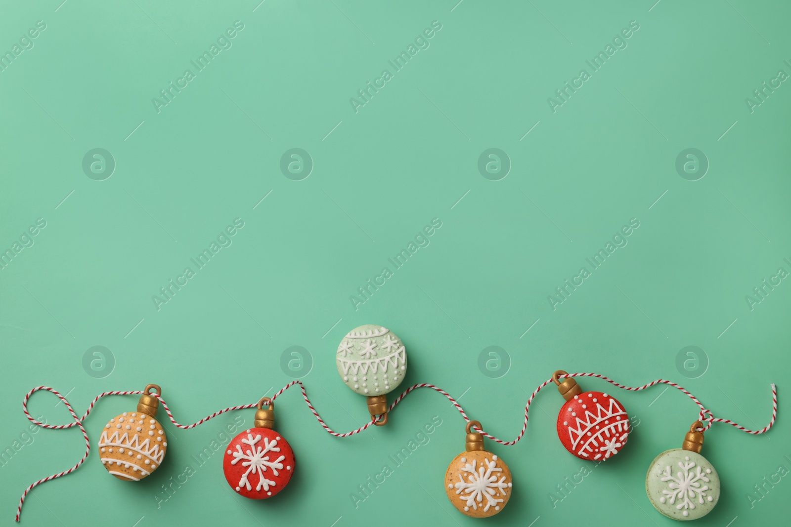 Photo of Beautifully decorated Christmas macarons with rope on turquoise background, flat lay. Space for text