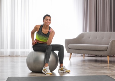Photo of Young woman doing exercise with dumbbells on fitness ball at home. Space for text