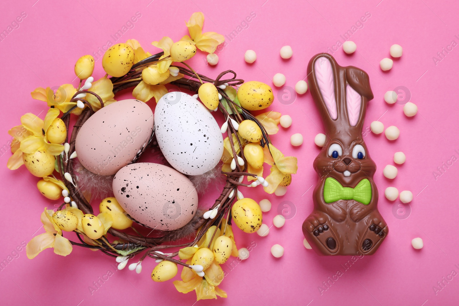 Photo of Flat lay composition with chocolate Easter bunny, festively decorated eggs and candies on pink background