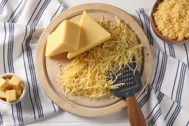 Photo of Grated, whole pieces of cheese and grater on white wooden table, flat lay