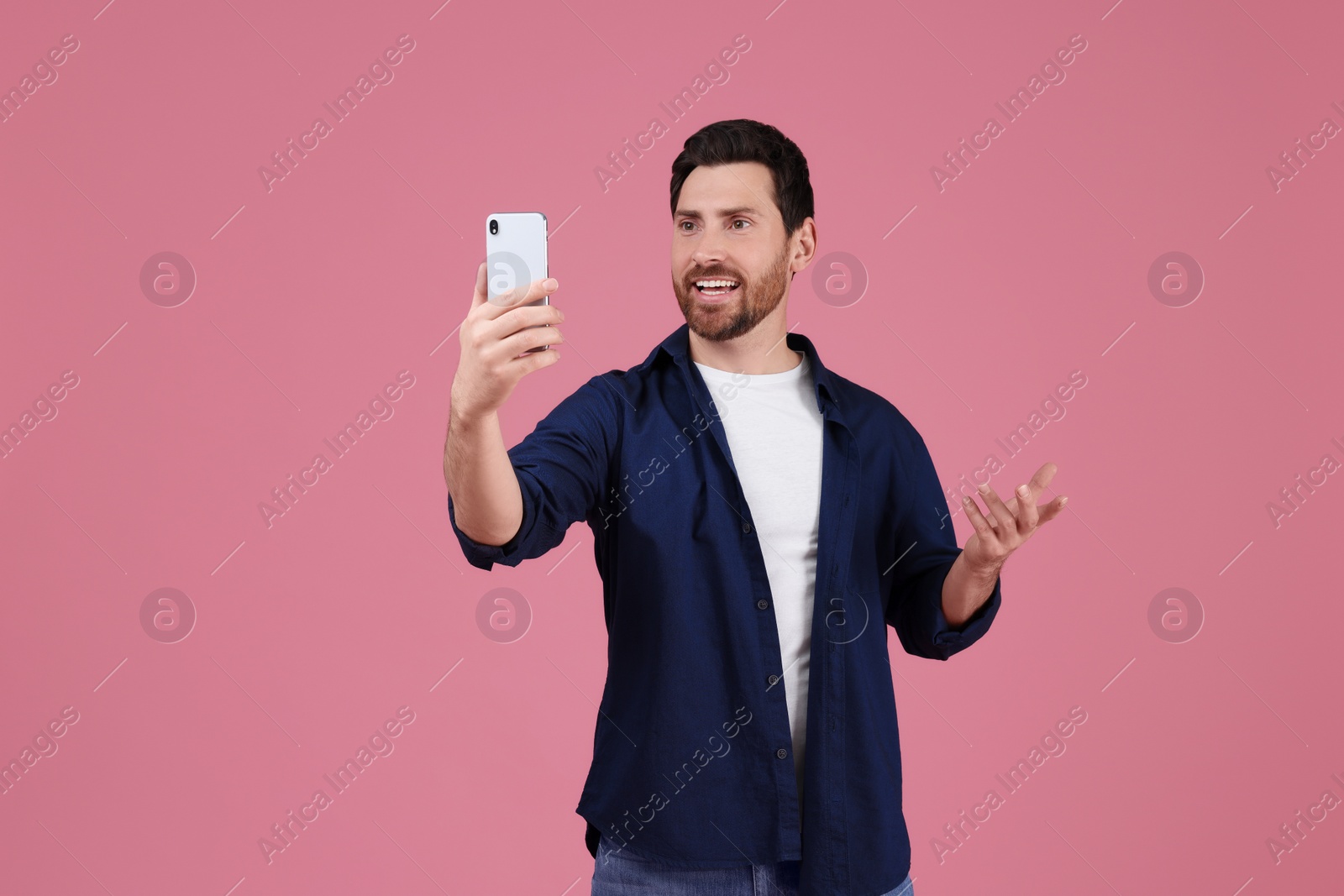 Photo of Smiling man taking selfie with smartphone on pink background, space for text