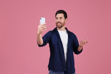 Photo of Smiling man taking selfie with smartphone on pink background, space for text