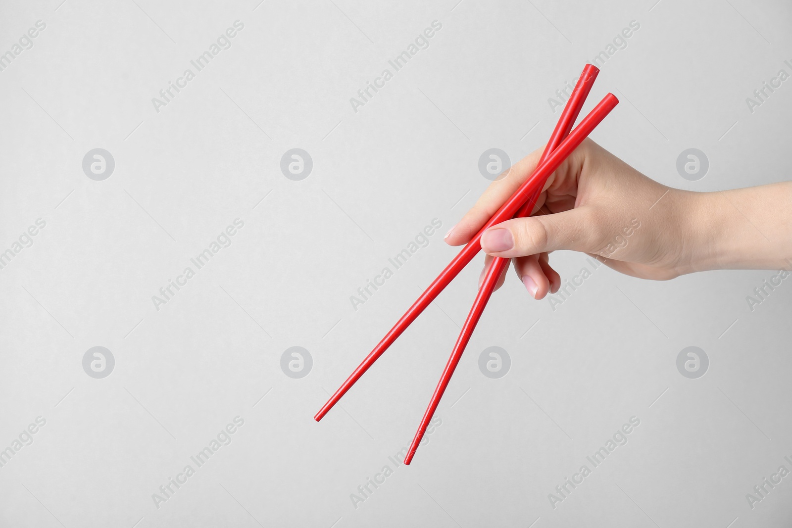 Photo of Woman holding pair of red chopsticks on light grey background, closeup. Space for text