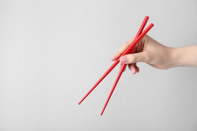 Photo of Woman holding pair of red chopsticks on light grey background, closeup. Space for text