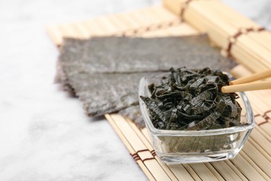 Photo of Chopped nori sheets with chopsticks on white marble table, closeup. Space for text