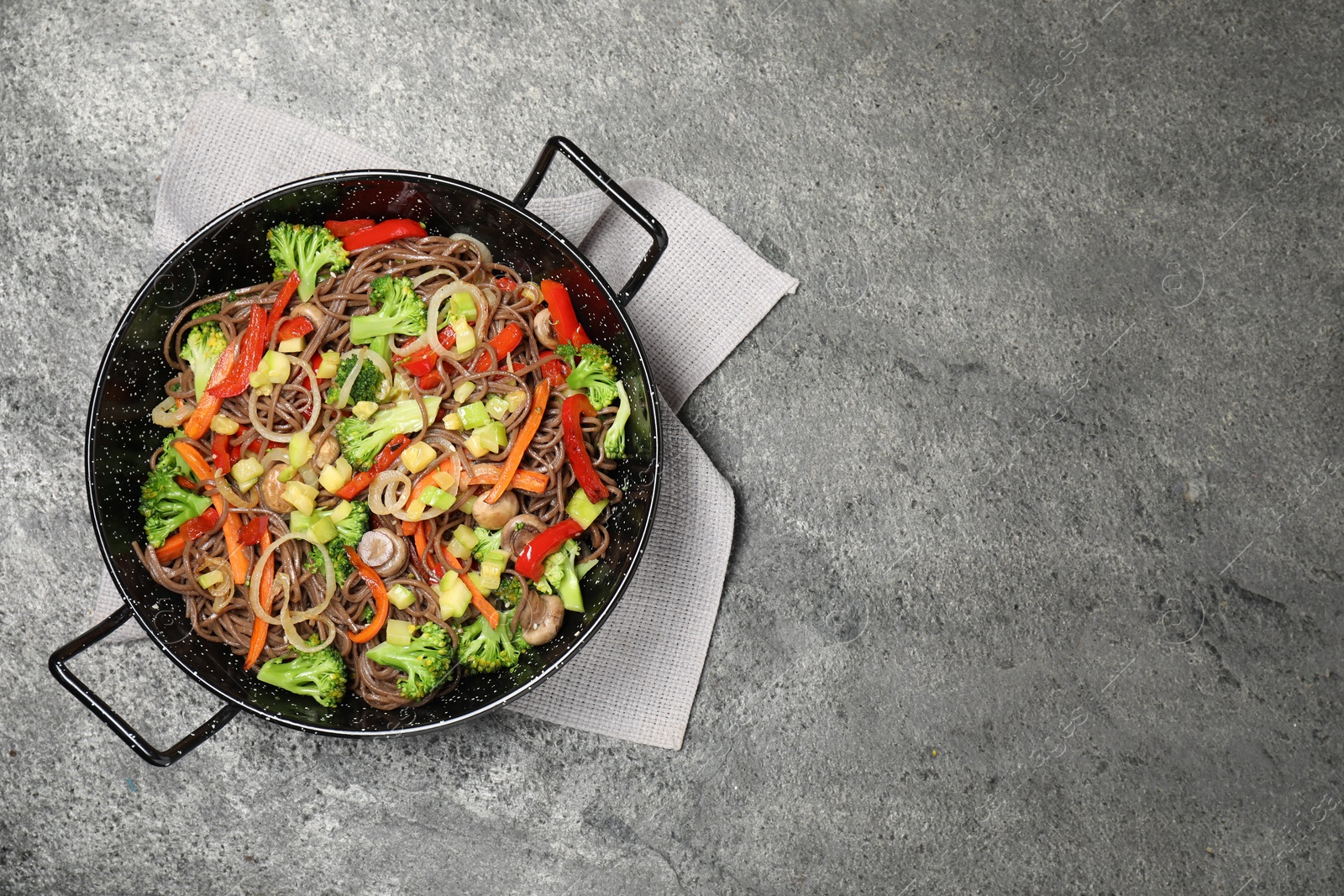 Photo of Stir fried noodles with mushrooms and vegetables in wok on grey table, top view. Space for text