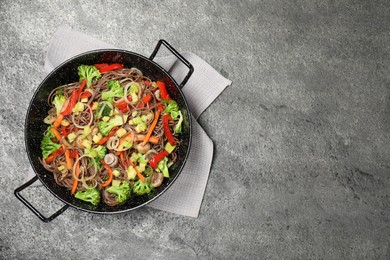 Stir fried noodles with mushrooms and vegetables in wok on grey table, top view. Space for text