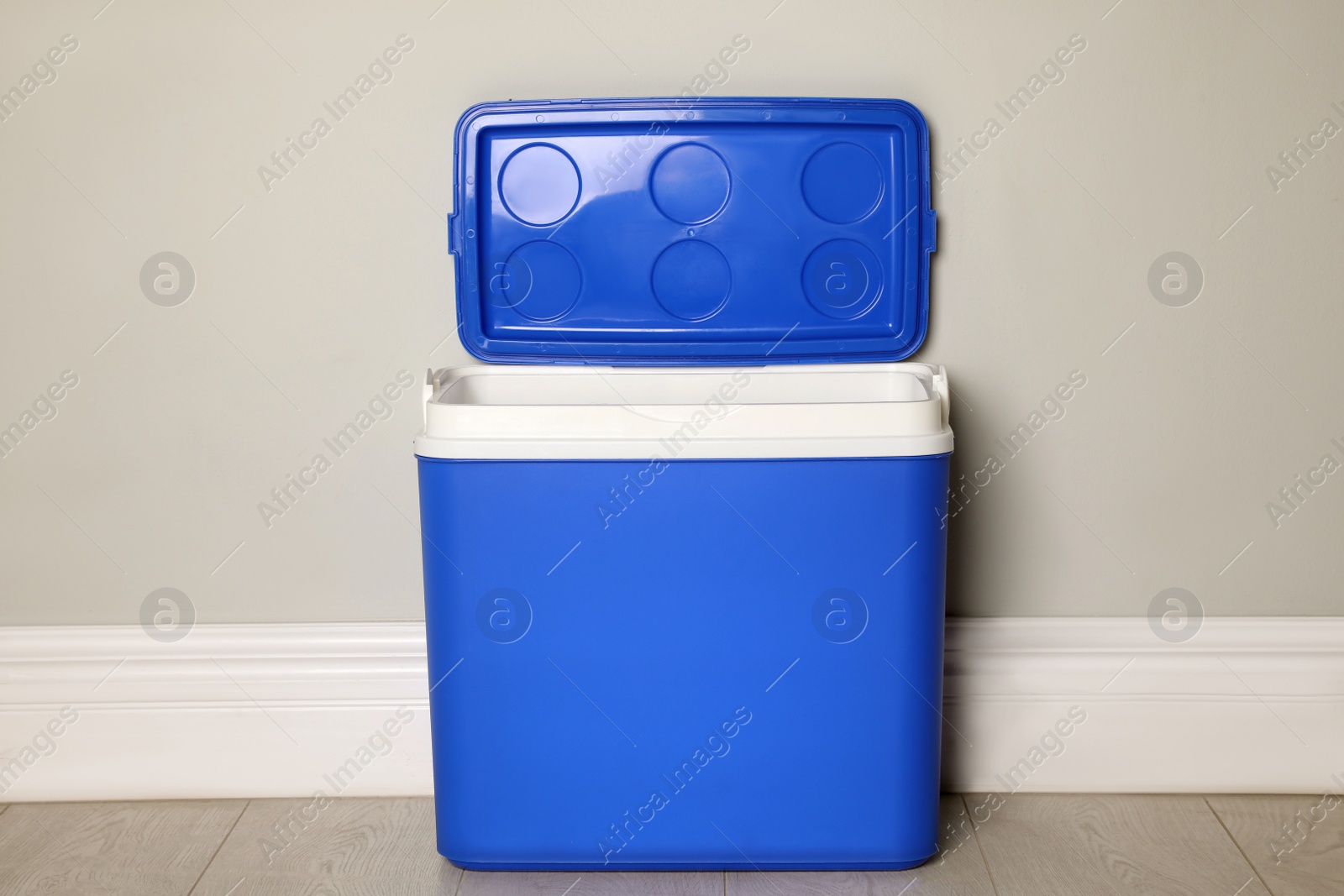 Photo of Open blue plastic cool box near light grey wall indoors