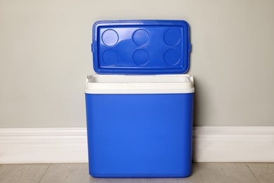 Photo of Open blue plastic cool box near light grey wall indoors