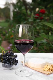 Glass of red wine and snacks served on white marble table outdoors