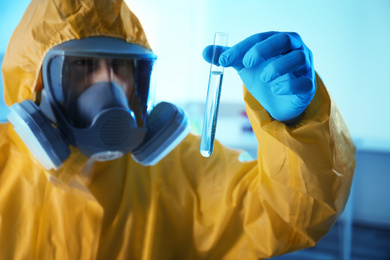 Scientist in chemical protective suit with test tube at laboratory, focus on hand. Virus research