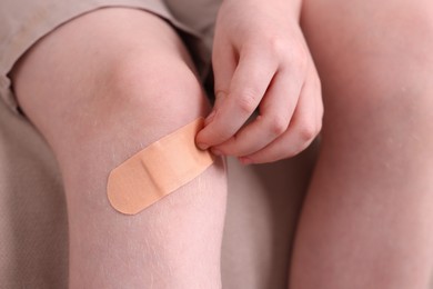 Photo of Little boy putting sticking plaster onto knee on sofa, closeup