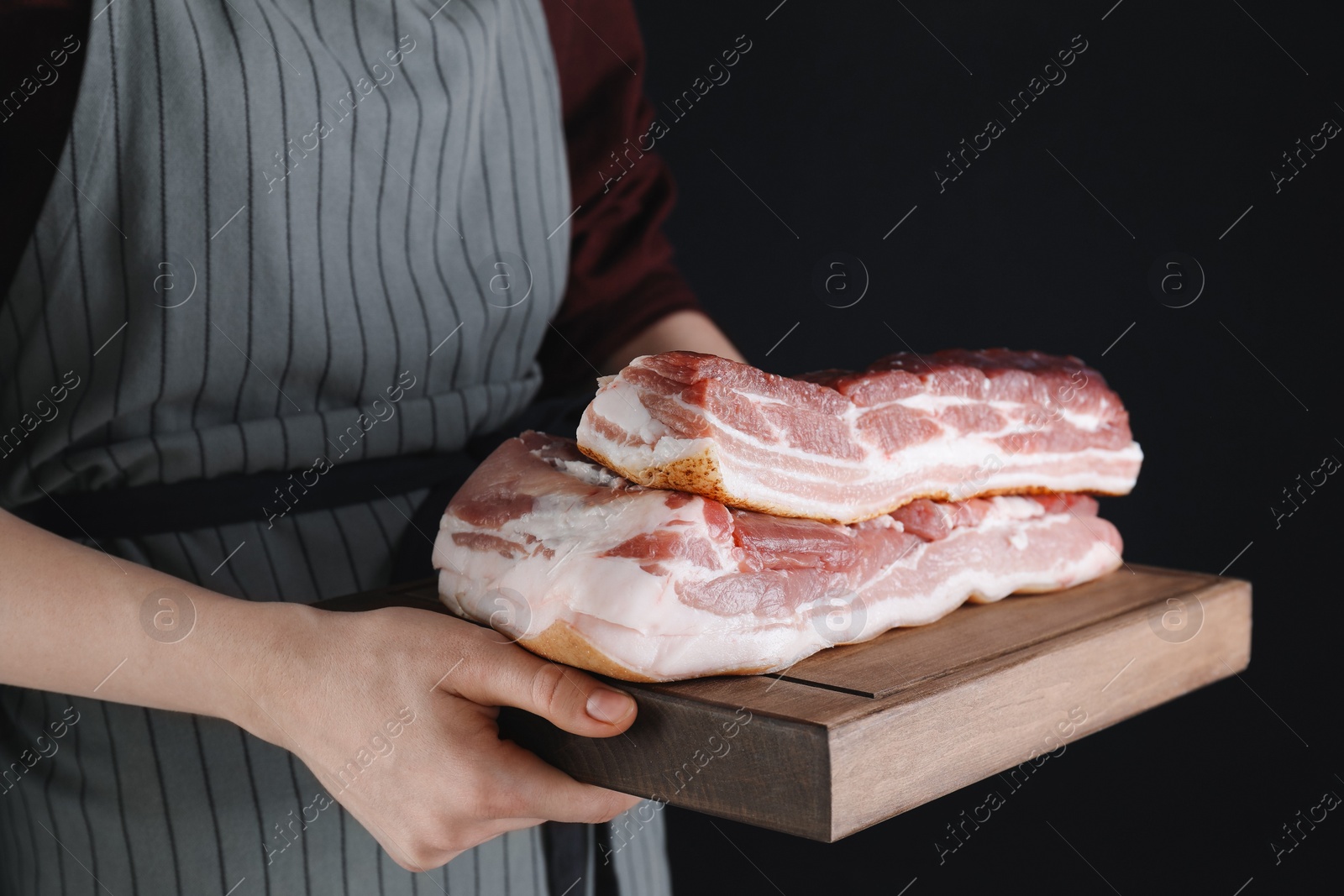 Photo of Woman holding wooden board with pieces of raw pork belly on black background, closeup