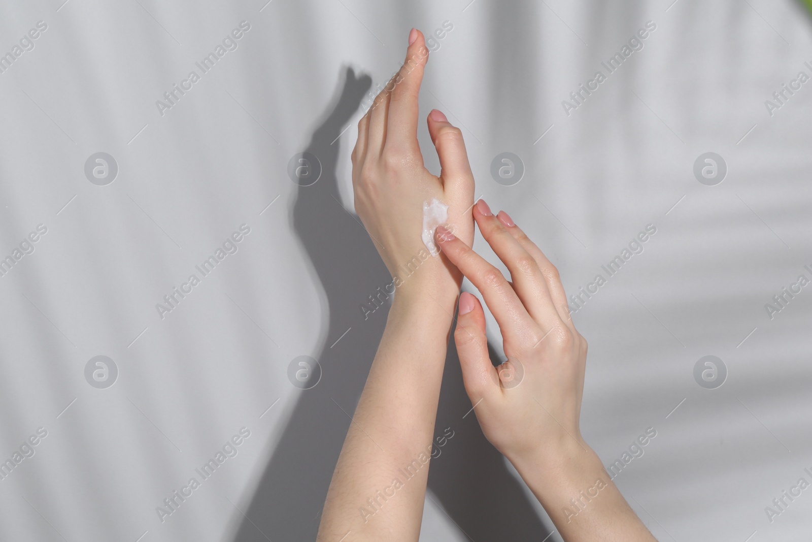 Photo of Woman applying cream on her hand against grey background, closeup