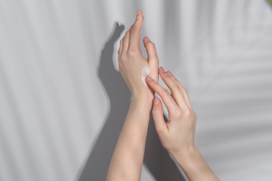 Photo of Woman applying cream on her hand against grey background, closeup