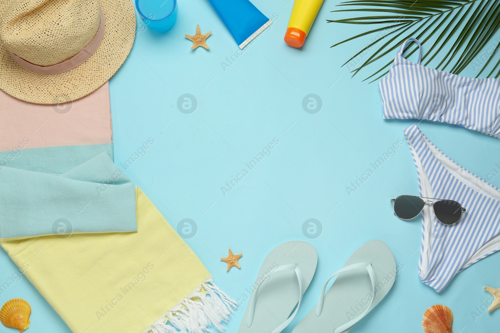 Photo of Frame of towel and different beach accessories on light blue background, flat lay. Space for text