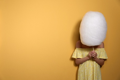 Young woman hiding behind tasty cotton candy on yellow background. Space for text