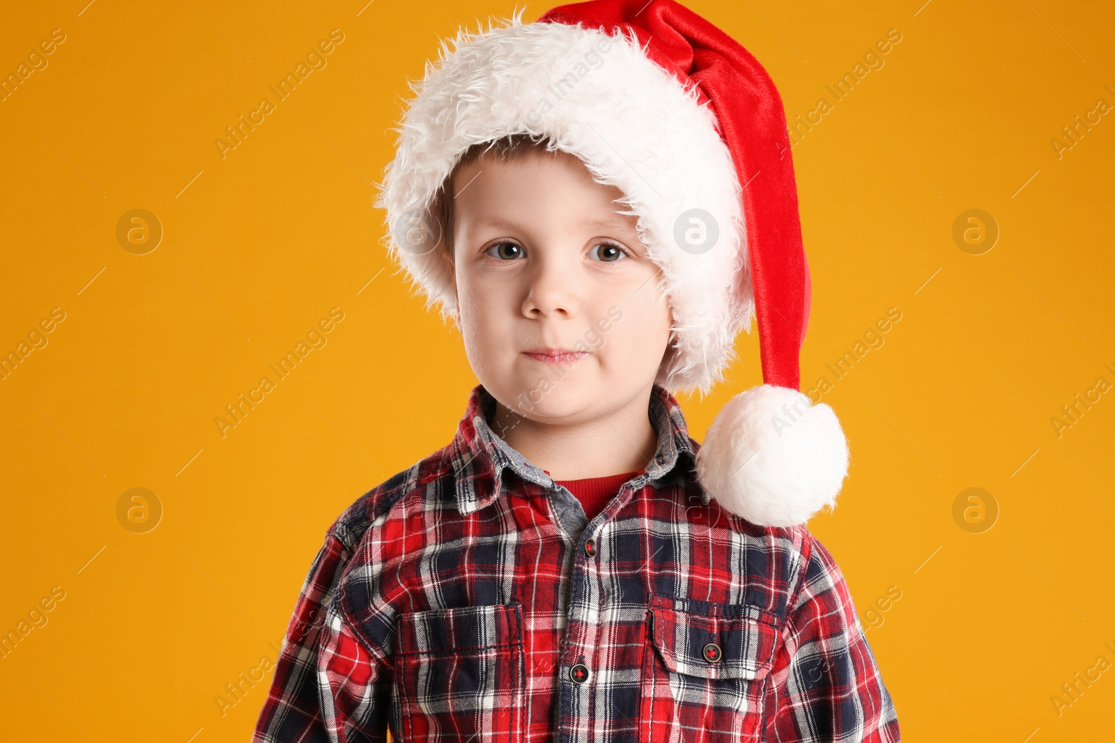 Photo of Cute child in Santa hat on yellow background. Christmas celebration