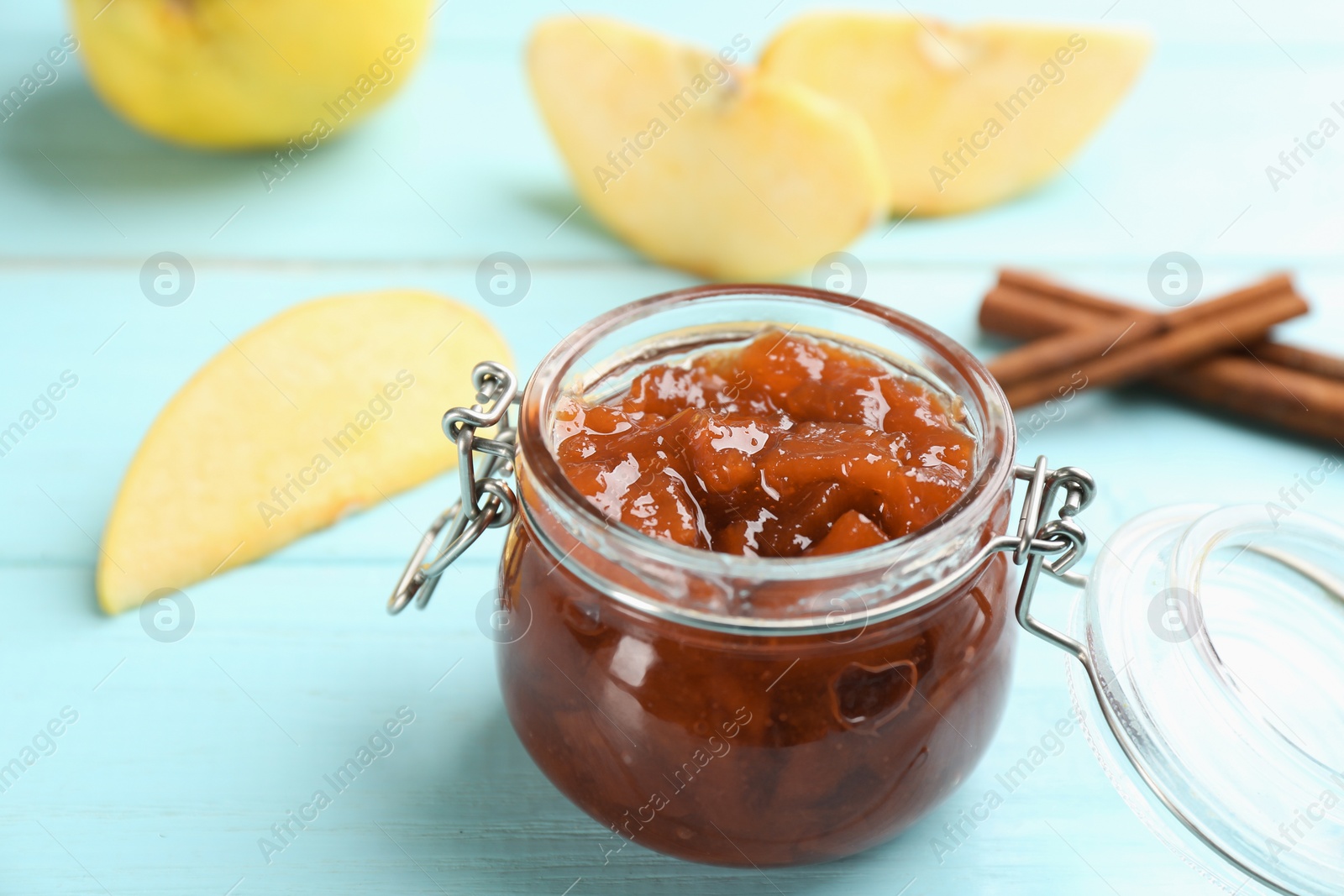 Photo of Delicious quince jam, fruits and cinnamon on light blue wooden table