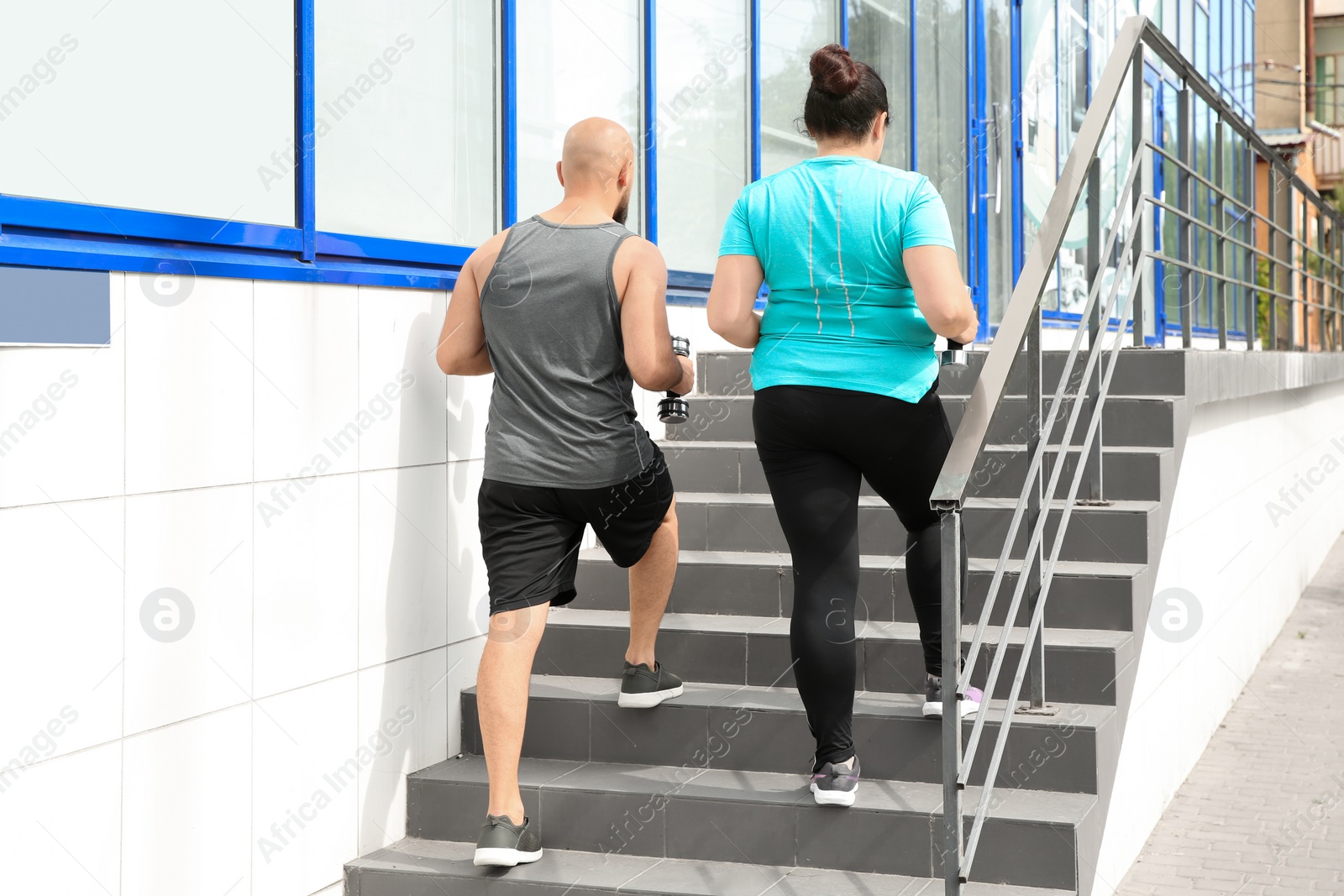 Photo of Overweight man and woman running with dumbbells on stairs outdoors