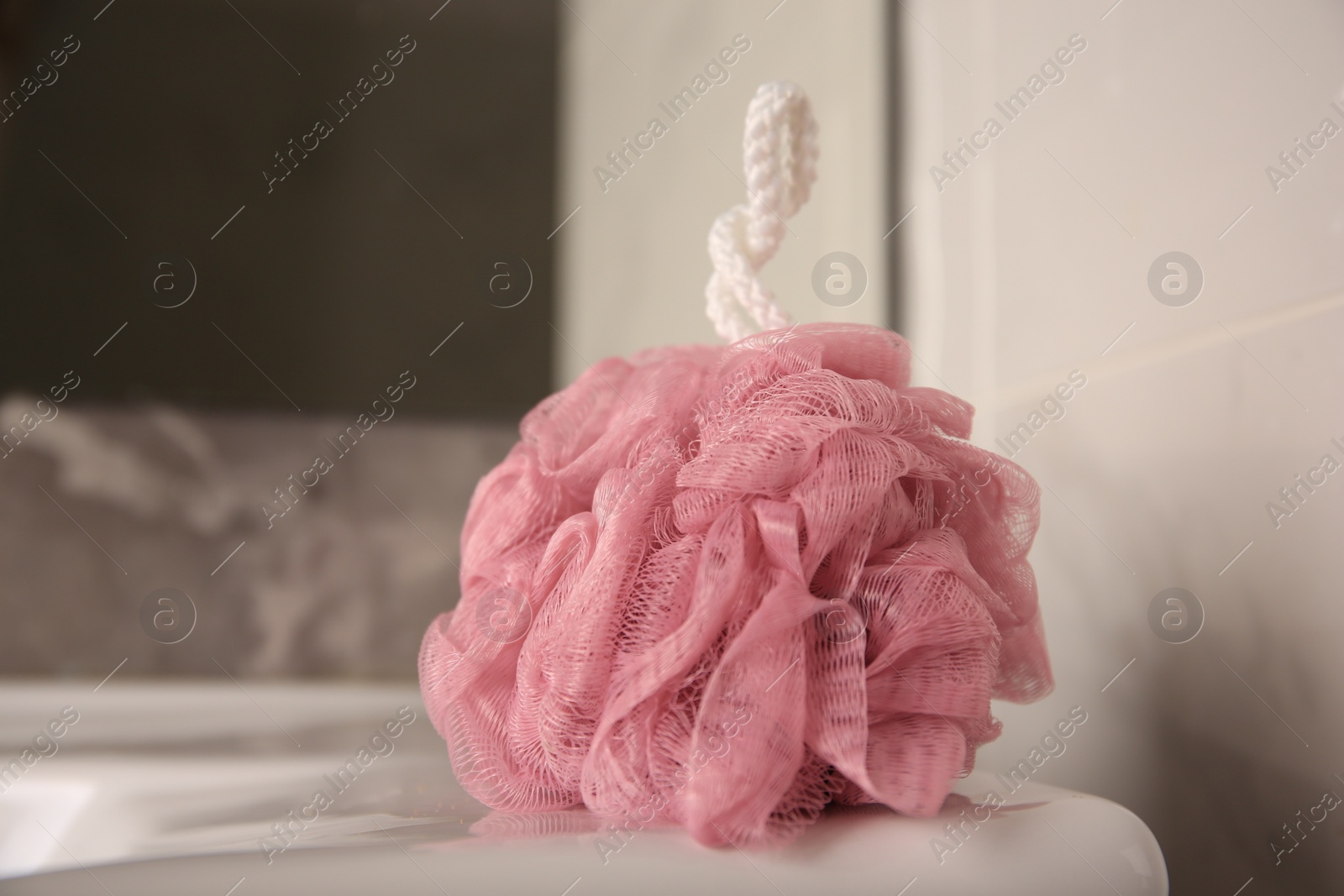 Photo of Pink shower puff on washbasin in bathroom, closeup