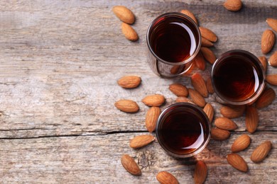 Photo of Shot glasses with tasty amaretto liqueur and almonds on wooden table, flat lay. Space for text