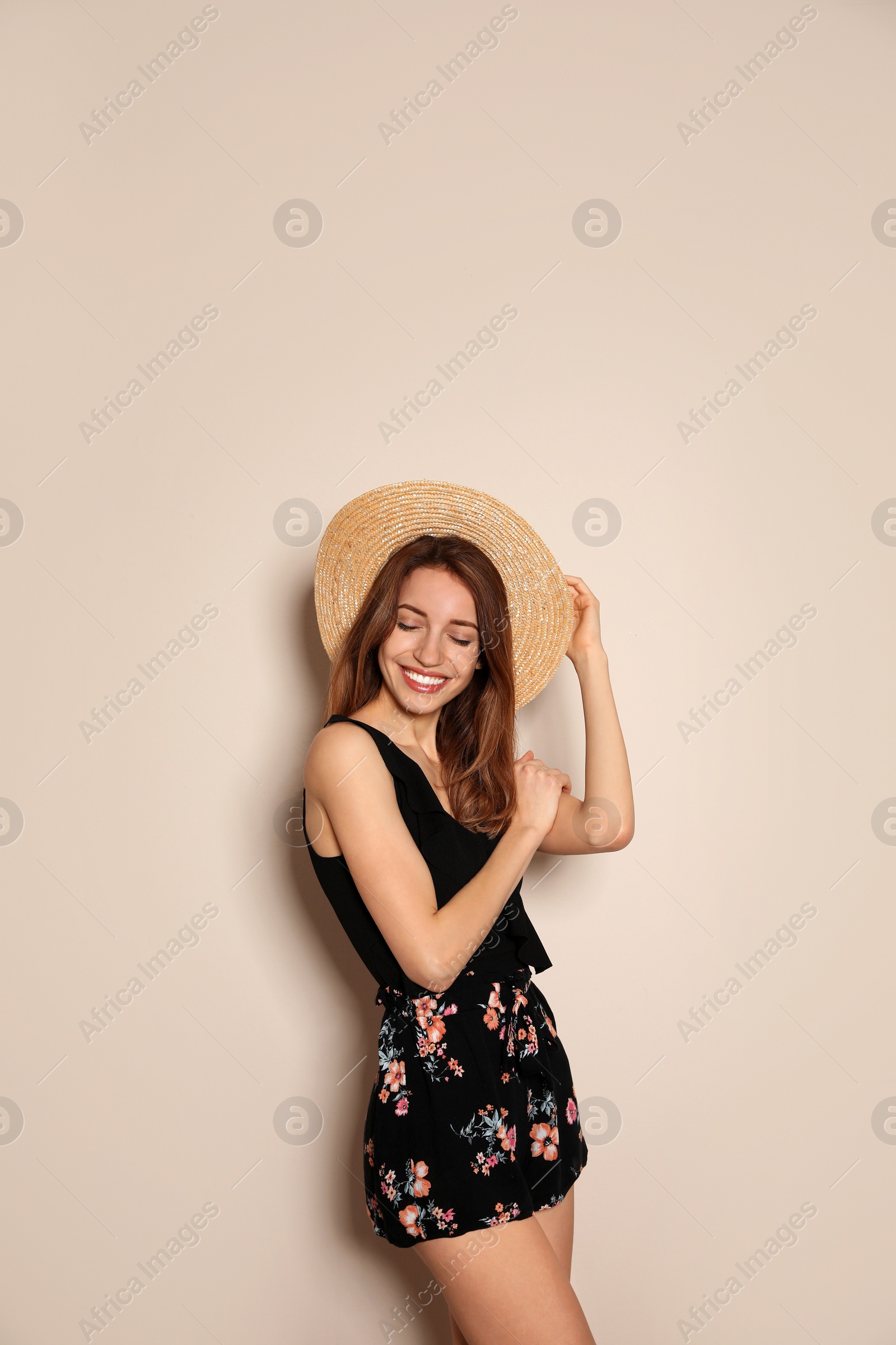 Photo of Young woman wearing floral print shorts and straw hat on beige background