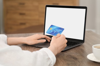 Woman with credit card using laptop for online shopping at wooden table indoors, closeup