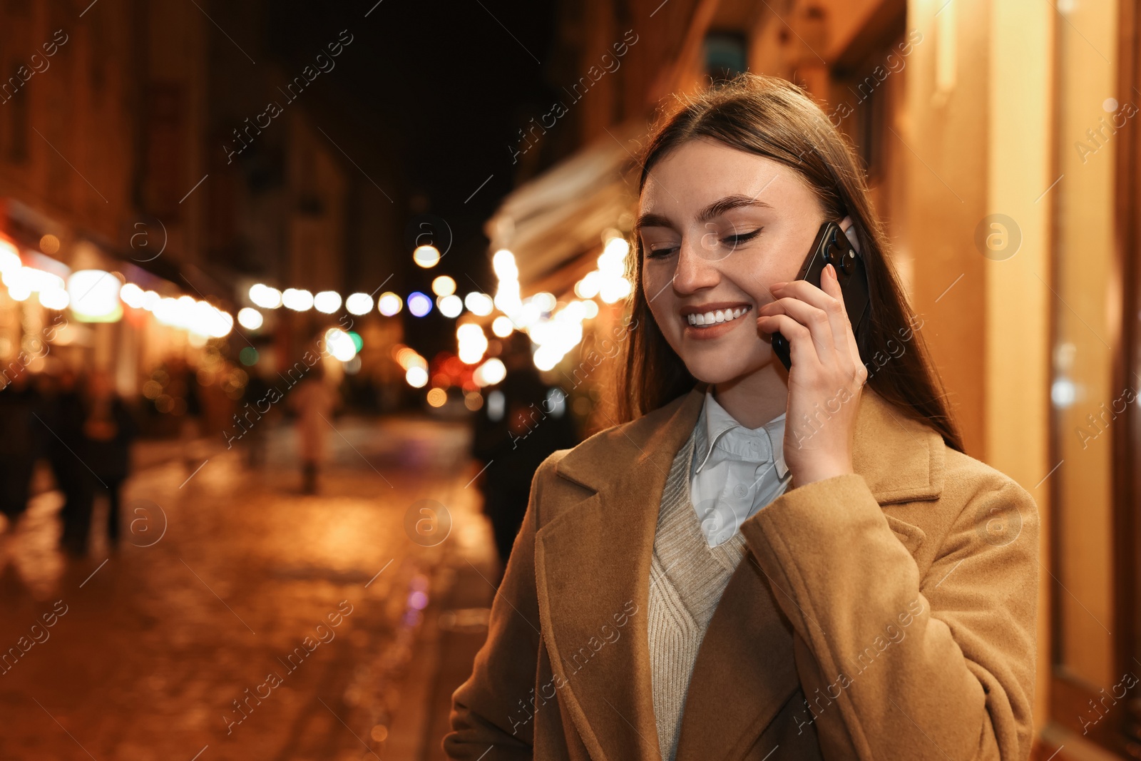 Photo of Smiling woman talking by smartphone on night city street. Space for text