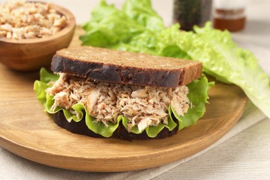 Photo of Delicious sandwich with tuna and lettuce leaves on wooden plate, closeup