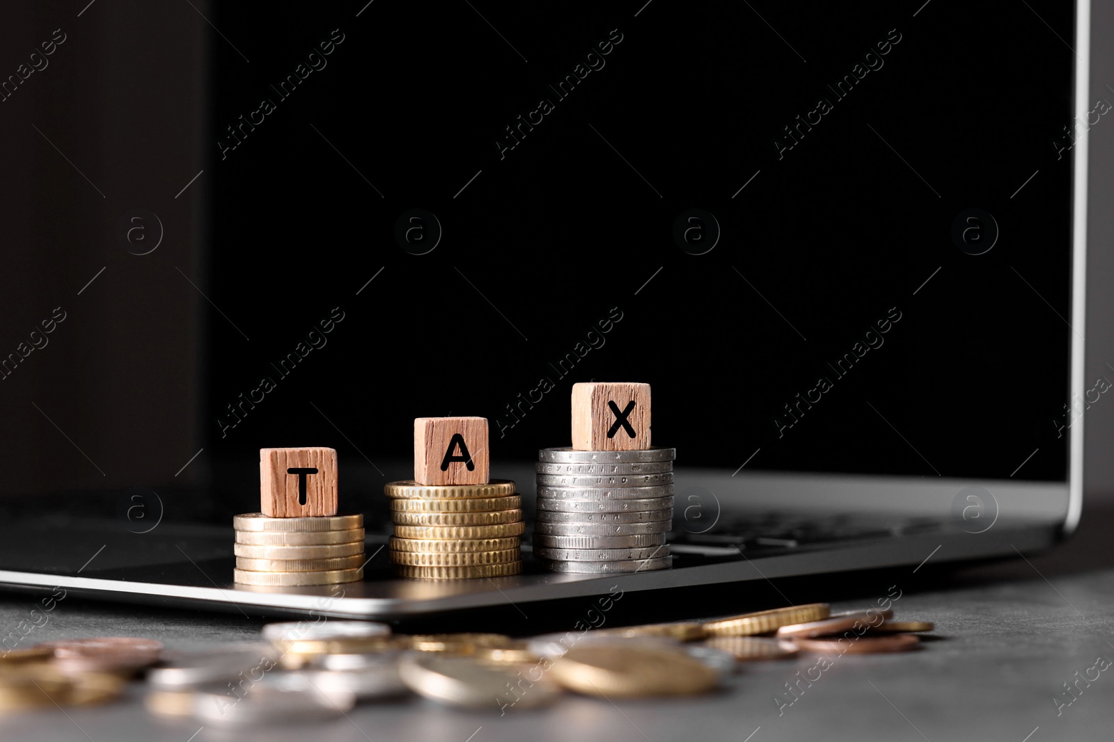 Photo of Word Tax made of wooden cubes, laptop and coins at grey table, space for text